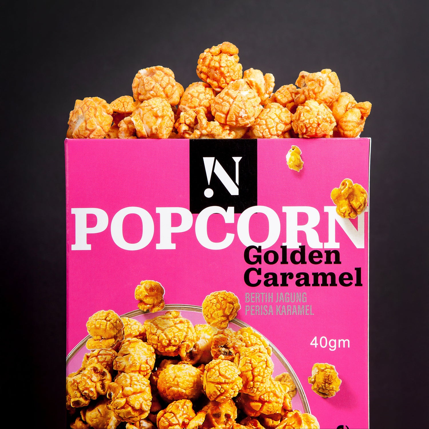 Pink box of Golden Caramel popcorn with popcorn spilling out on a black background