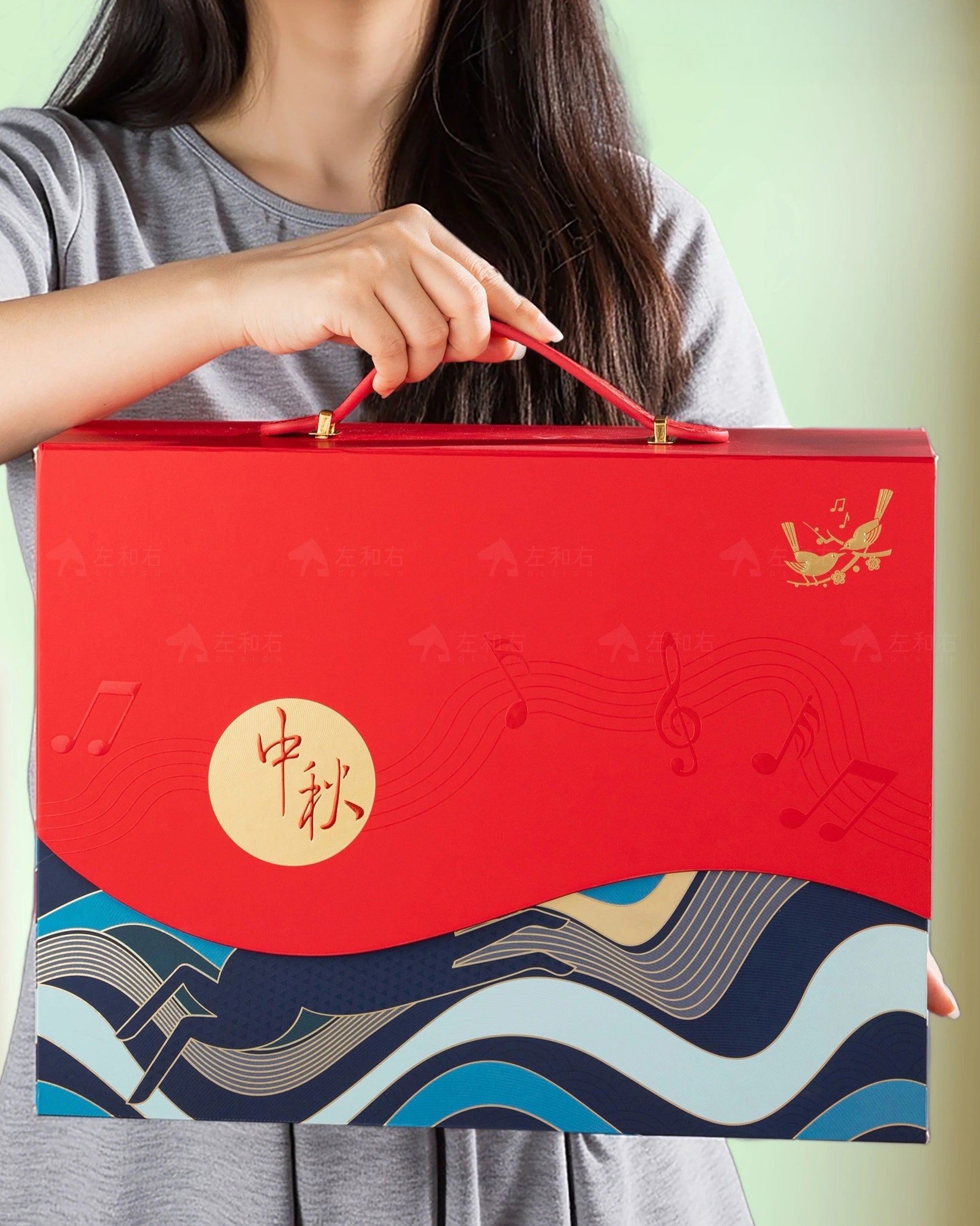 Person holding a red gift box with blue wave design and gold accents