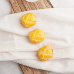 Three pineapple-shaped pastries on a white cloth with a wooden surface underneath.