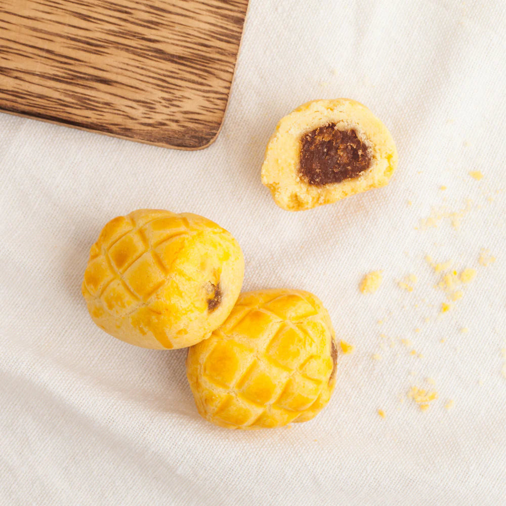 Three pineapple-shaped pastries on a white cloth with a wooden board in the background.