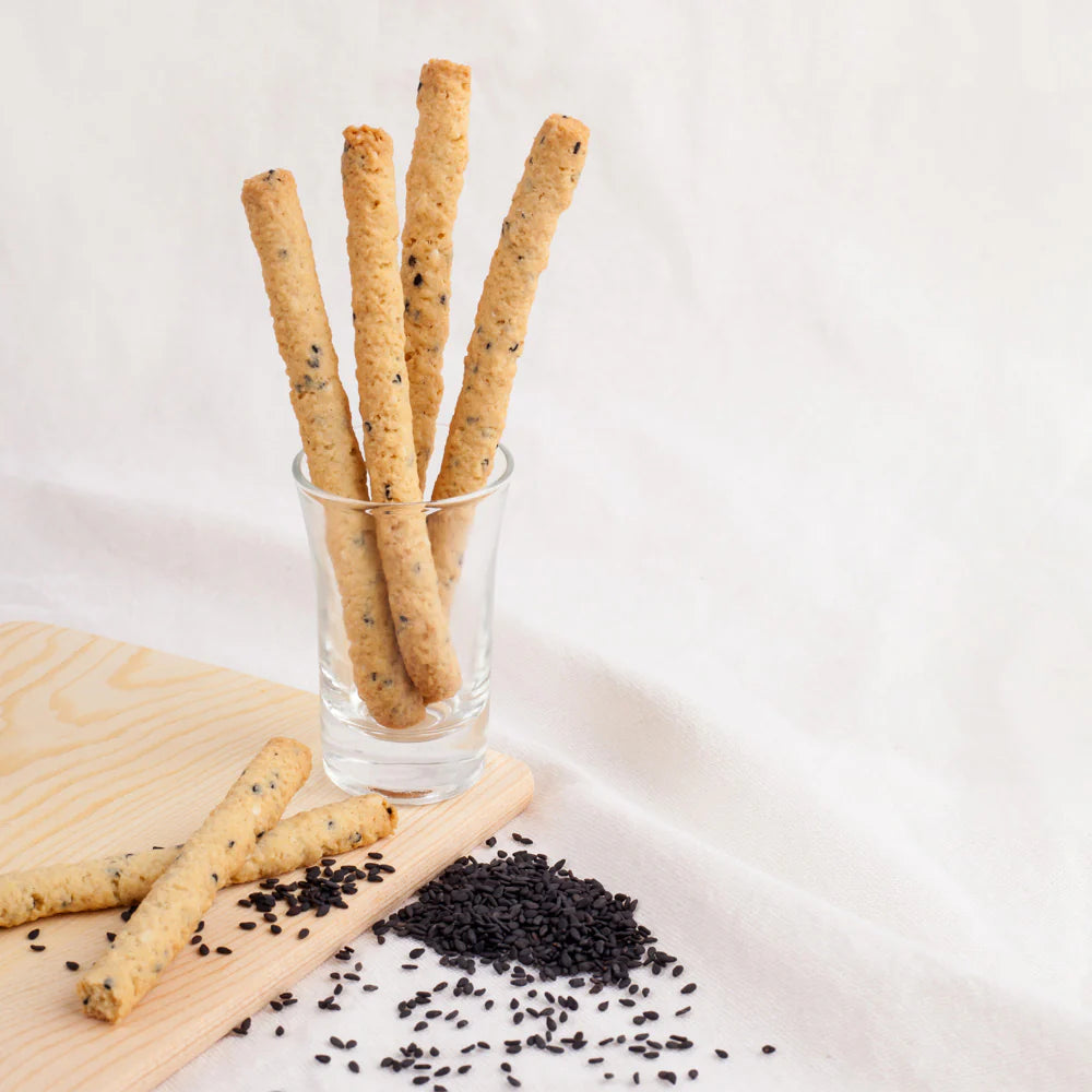 Glass with breadsticks and black seeds on a light background