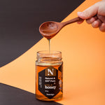 Hand holding a wooden spoon drizzling honey from a jar labeled 'Nostalgia' on an orange and black background.
