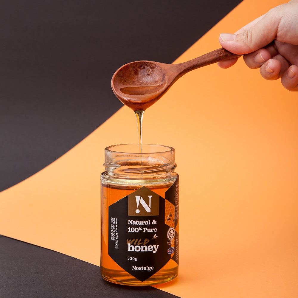 Hand holding a wooden spoon drizzling honey from a jar labeled 'Nostalgia' on an orange and black background.