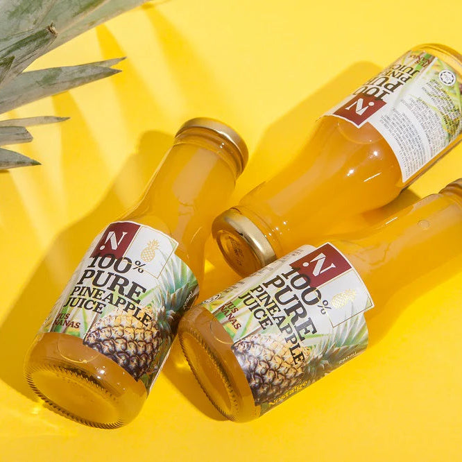 Three bottles of 100% pure pineapple juice on a yellow background with a pineapple leaf.