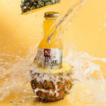 Bottle of pineapple juice being poured into a pineapple with water splashing around on a yellow background
