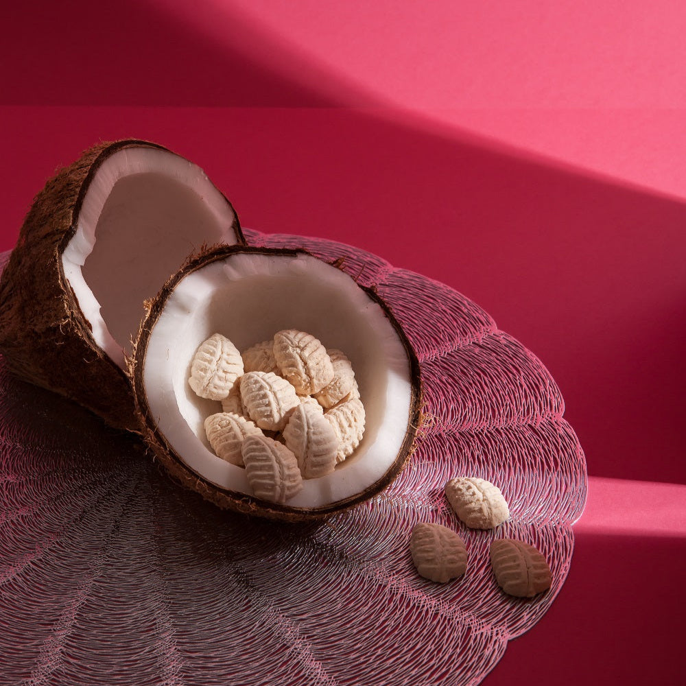 Coconut with white interior and small brown and white cookies on a pink background